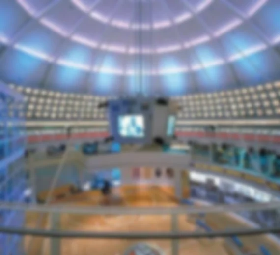 This is a background image for the New England Sports Museum's text. The photo shows an interior that looks like a stadium, with a wooden floor similar to a basketball court. The image is blurred out to facilitate reading the overlay text. 
