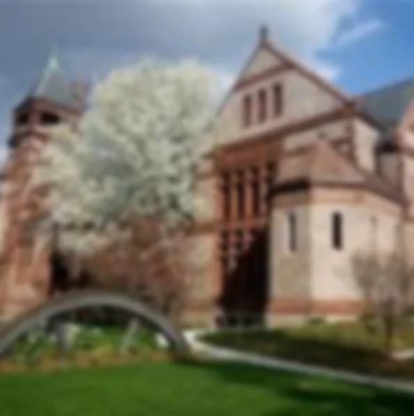 This is a background image for the Waterworks Museum text. It shows a large brick building with a tree in front of it and white flowers. The image is blurred out to facilitate reading the overlay text. 